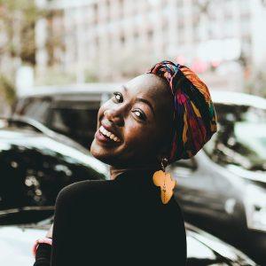 Black pride in Detroit and East St. Louis community gathering A joyful woman wearing a colorful headwrap and distinctive earrings, smiling in an urban setting.