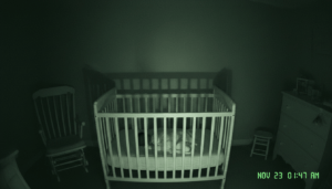 Night vision view of a nursery baby monitor showing a shadow moving near a crib